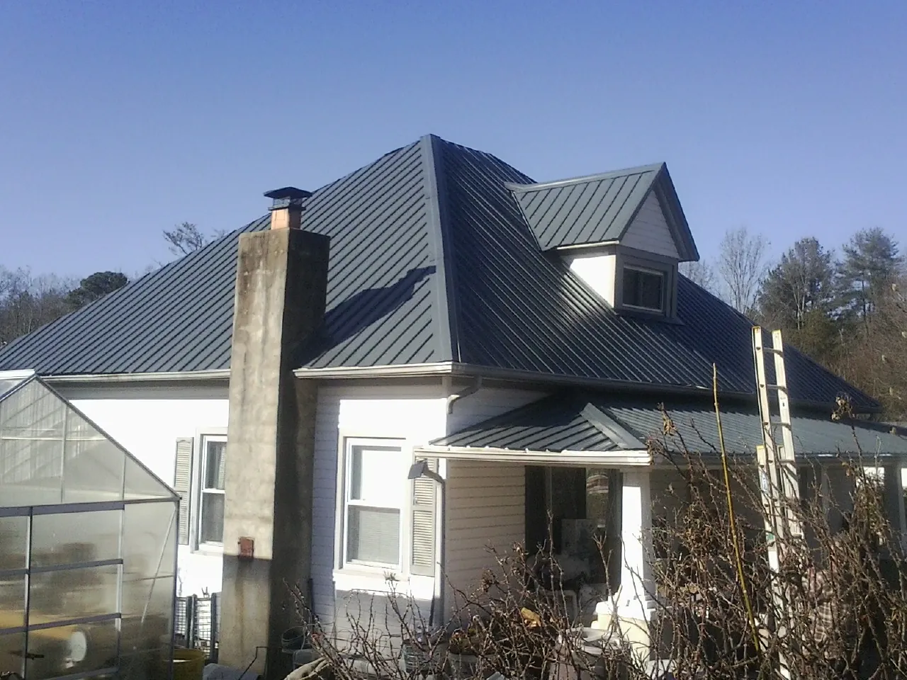 Dark blue standing seam metal roof on a white farmhouse with dormer — Slate & Tile Roof Repair by Roofing Brothers in Helendale