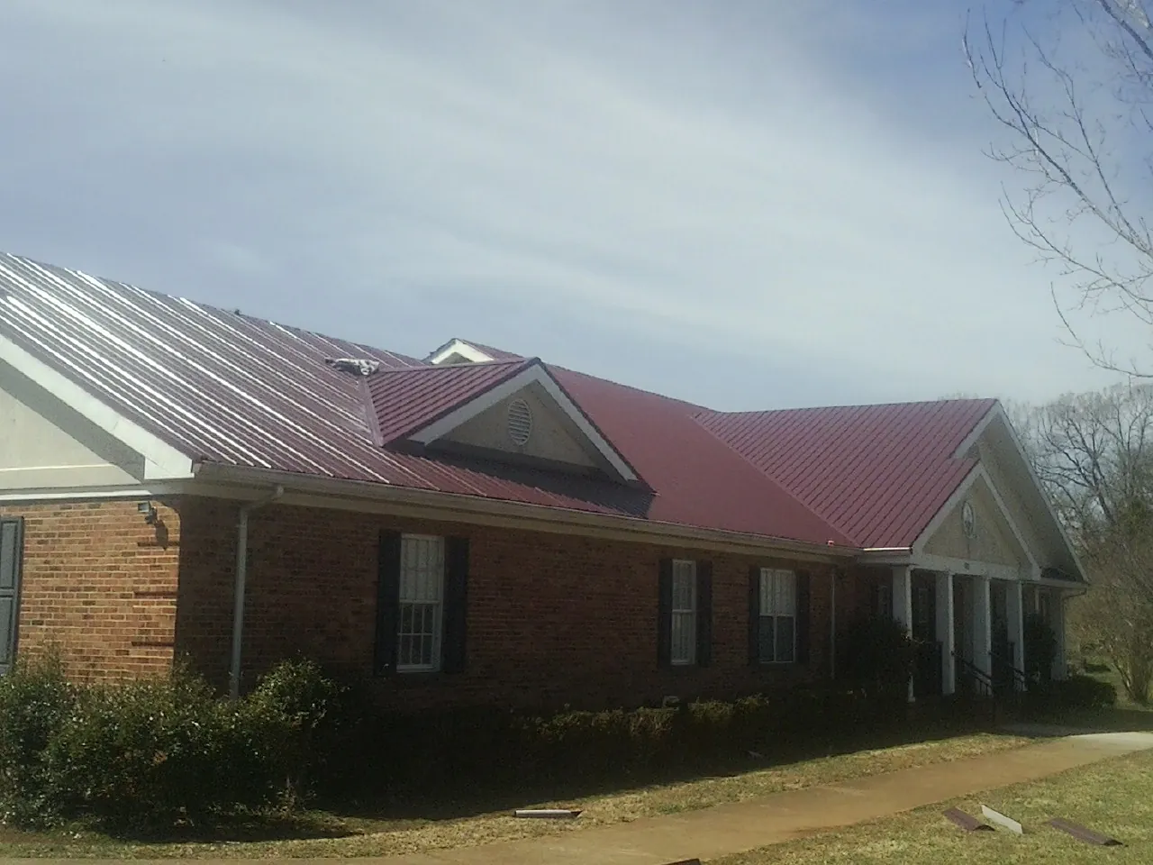 Red metal roof with gabled entries on a long brick building, from a Hail Damage Roof Repair job in Helendale