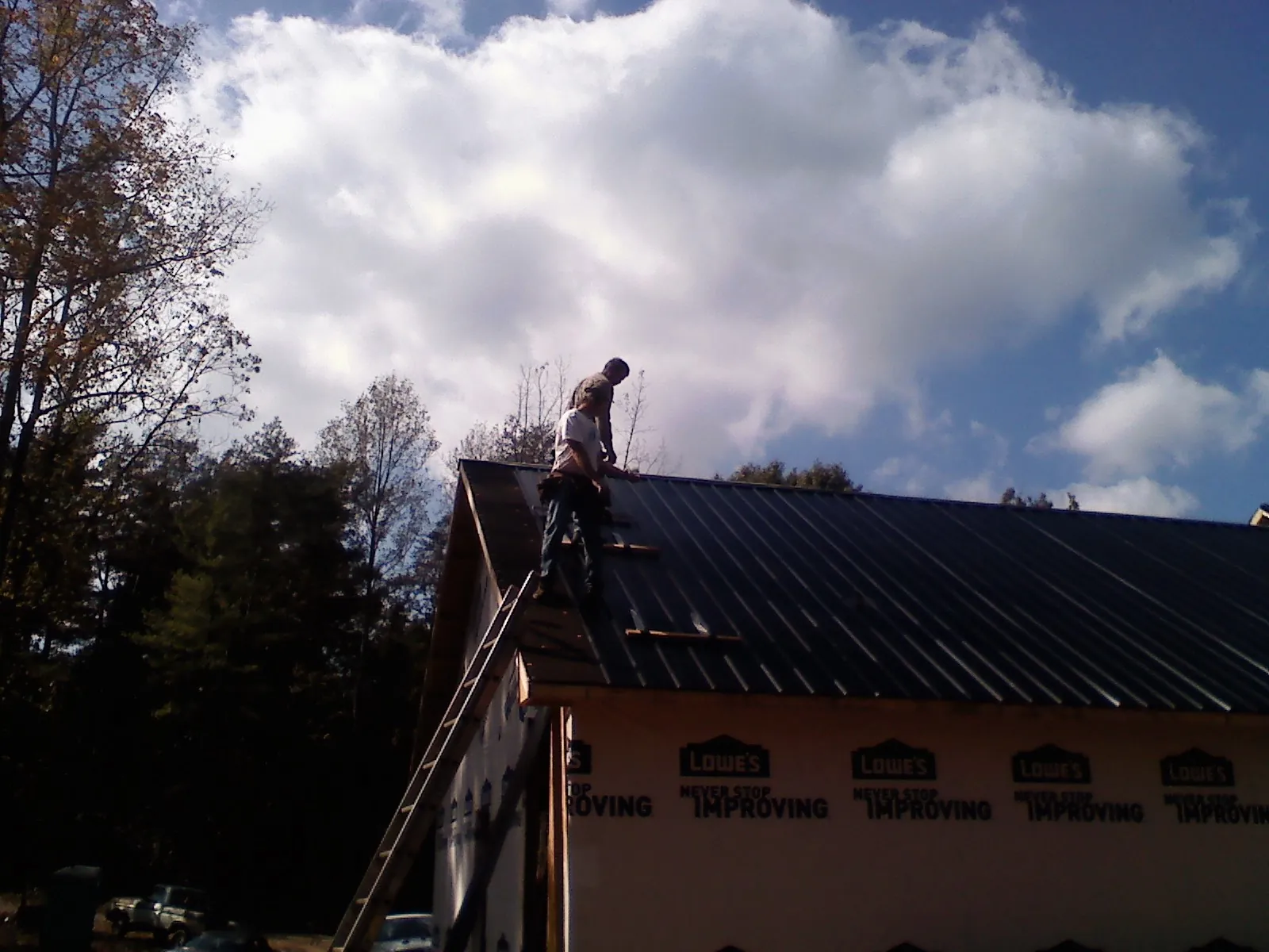 Roofer fastening dark metal panels high against a cloudy sky, from a Roof Inspection job in Helendale
