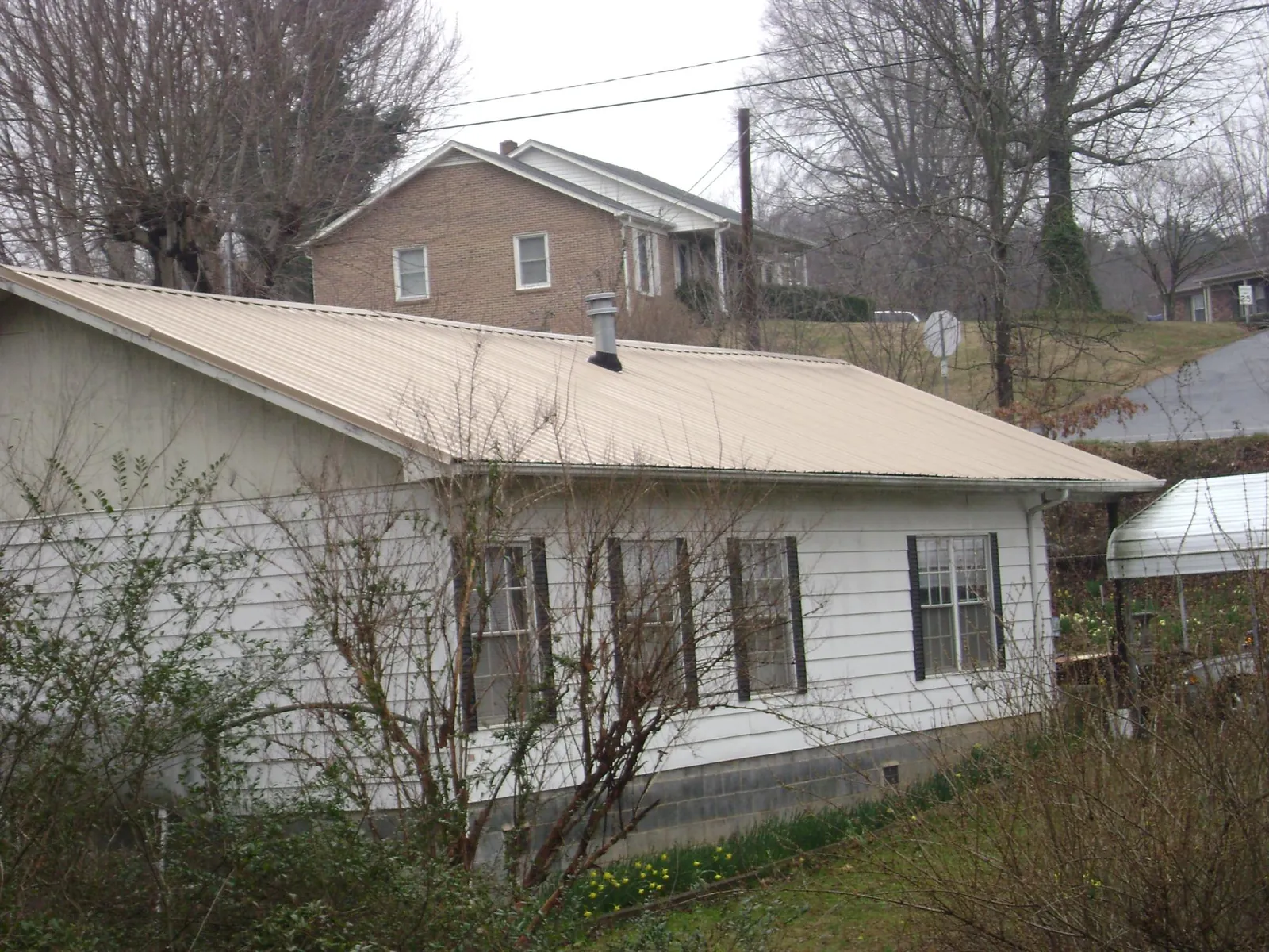 Tan metal roof on a white sided house set into a hillside — Commercial Roofing by Roofing Brothers in Helendale