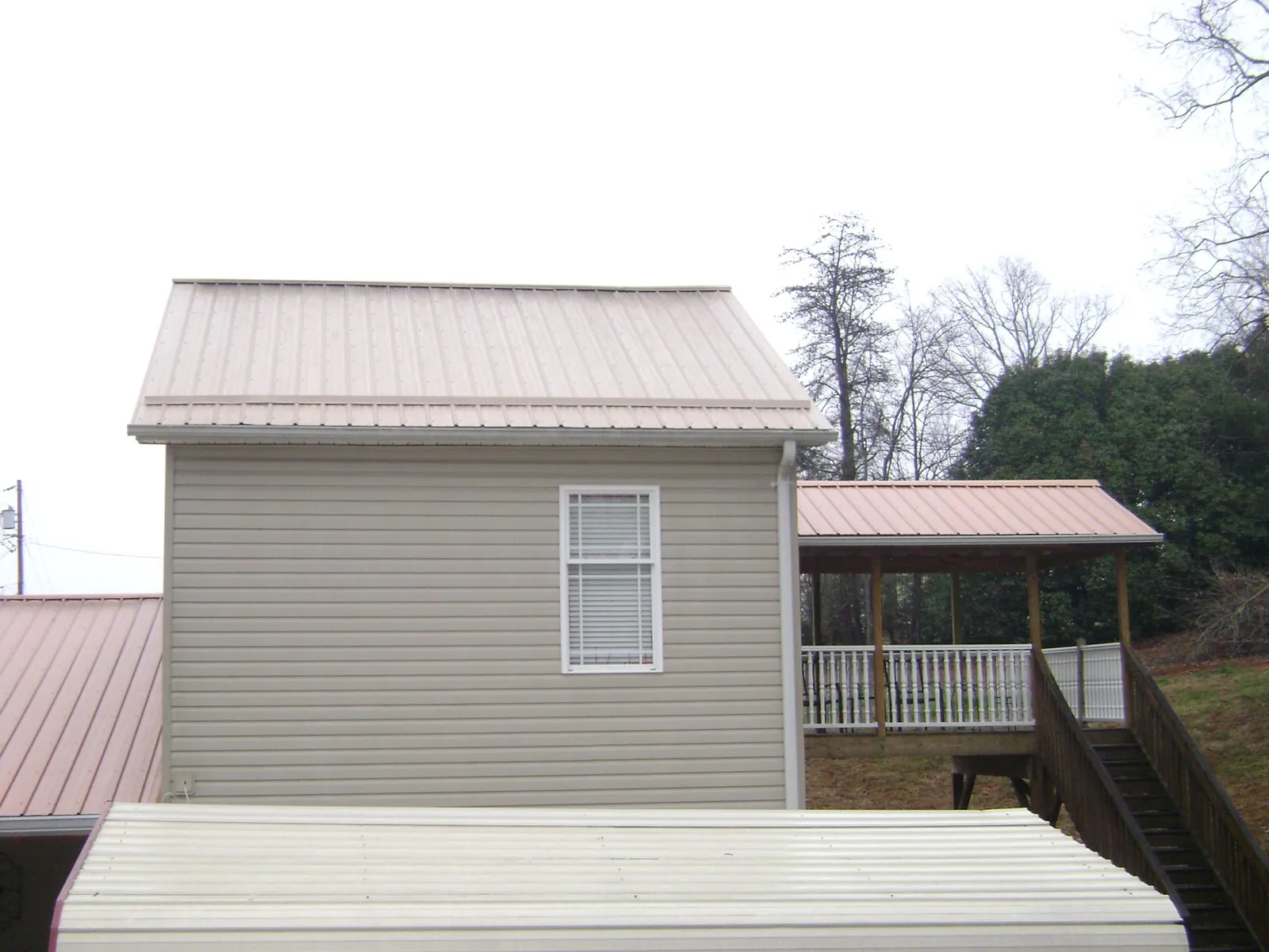 Tan metal roofs on a two story addition and attached porch, from a Roof Replacement job in Helendale